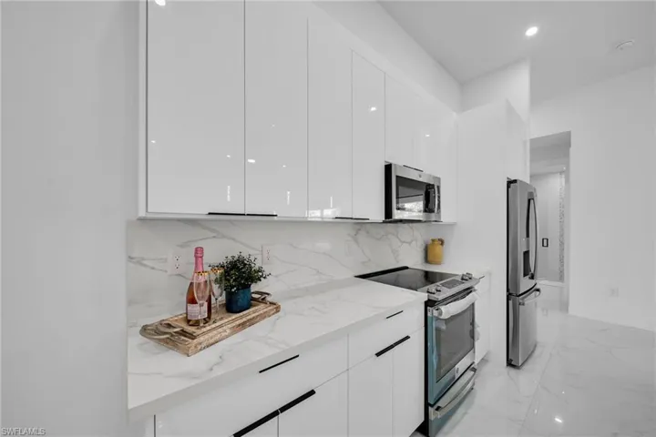 Kitchen with stainless steel appliances, modern cabinets, white cabinetry, light stone countertops, and decorative backsplash