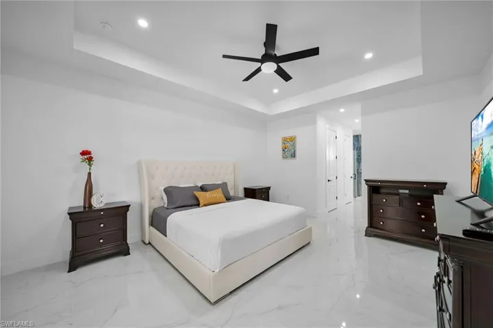 Bedroom featuring a raised ceiling, recessed lighting, light marble finish flooring, baseboards, and ceiling fan