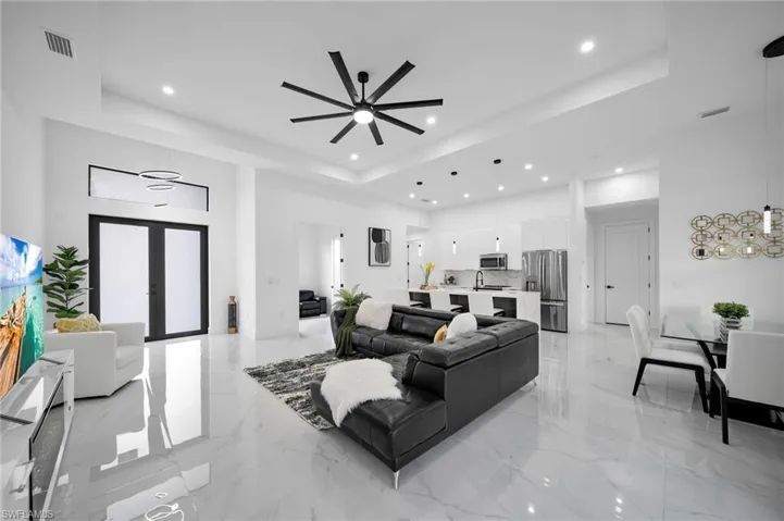 Living room with a raised ceiling, recessed lighting, light marble finish floors, and a ceiling fan