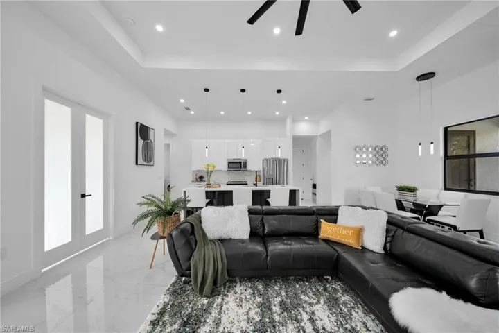 Living room with a ceiling fan, recessed lighting, a raised ceiling, light marble finish flooring, and baseboards