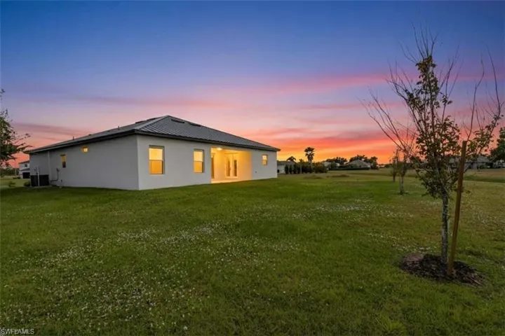 Back of house at dusk with a yard, stucco siding, and a patio