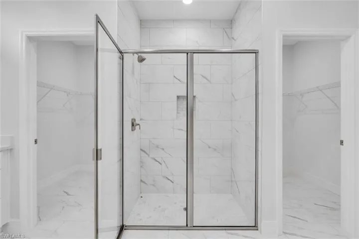 Full bath with a walk in closet, light marble finish flooring, and a stall shower