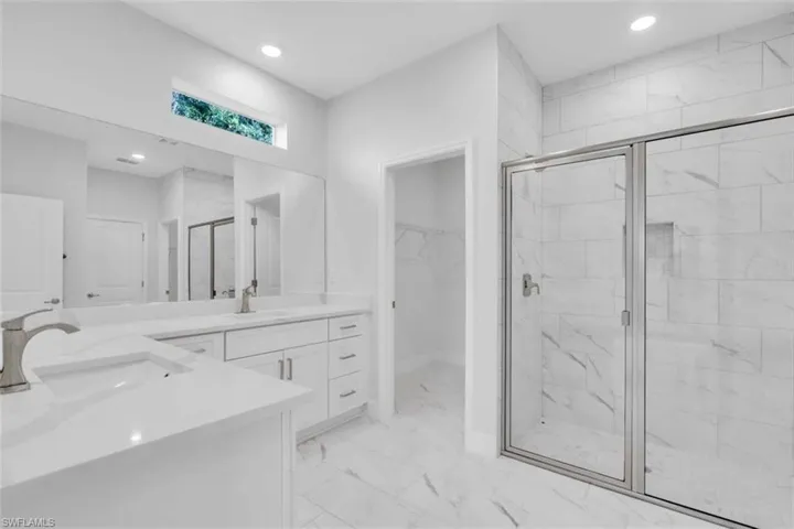 Bathroom featuring two vanities, a walk in closet, a stall shower, recessed lighting, and light marble finish floors