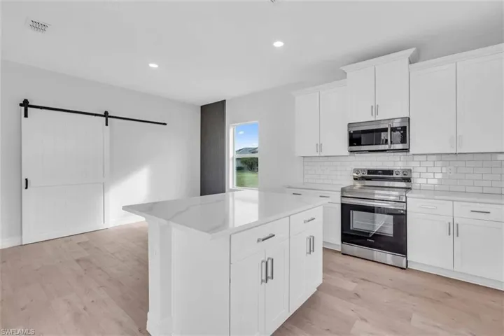 Kitchen/dining room featuring stainless steel appliances, white cabinetry, a barn door, decorative backsplash, and light wood finished floors