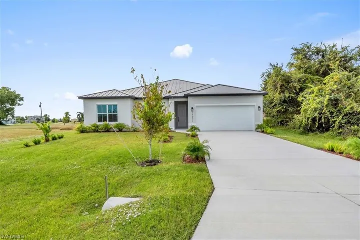 Ranch-style home with a garage, driveway, a metal roof, a standing seam roof, and stucco siding