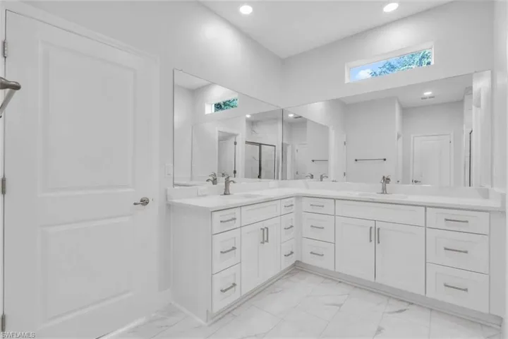 Bathroom with double vanity, a marble finish shower, light marble finish floors, and recessed lighting