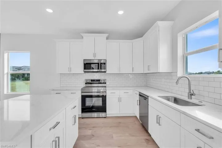 Kitchen with appliances with stainless steel finishes, white cabinets, light stone counters, light wood-type flooring, and recessed lighting