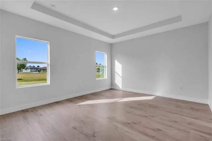 Primary bedroom with trey ceiling and light wood-type flooring