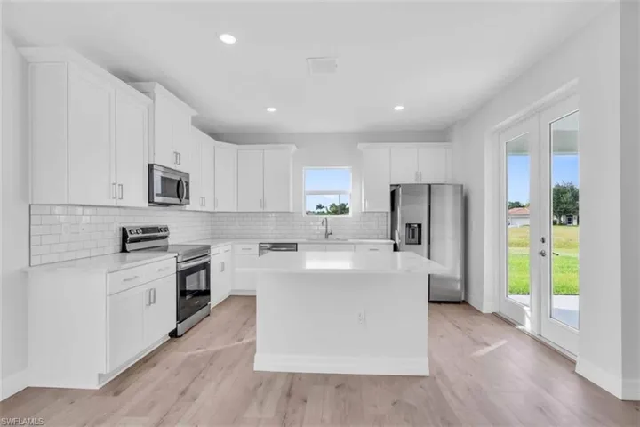 Kitchen featuring appliances with stainless steel finishes, tasteful backsplash, a center island, white cabinets, French doors that open up to the lanai/back porch and light wood-type flooring