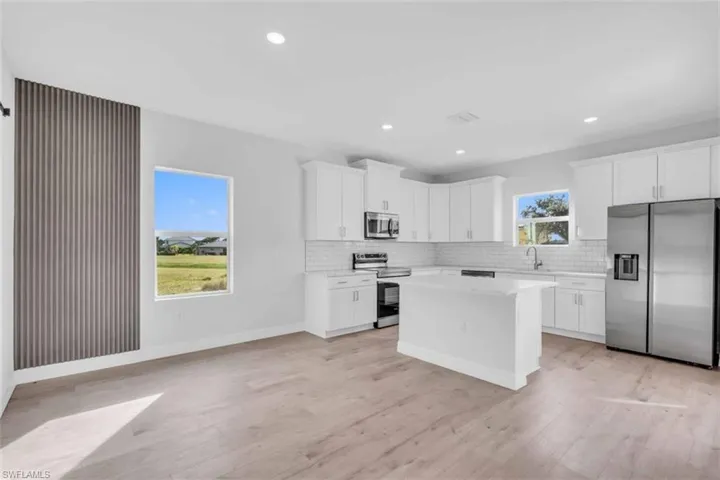 Kitchen/dining room featuring stainless steel appliances, decorative backsplash, a center island, white cabinetry, and light wood finished floors