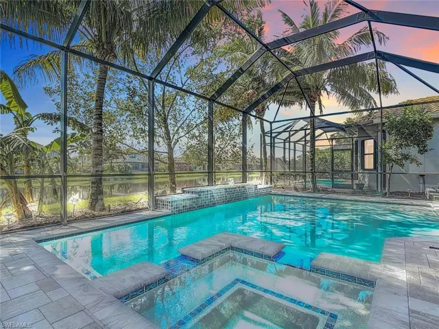 Pool at dusk with an in ground hot tub, a water view, and a lanai