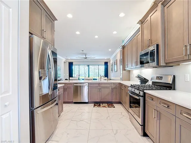 Kitchen with kitchen peninsula, ceiling fan, sink, crown molding, and stainless steel appliances