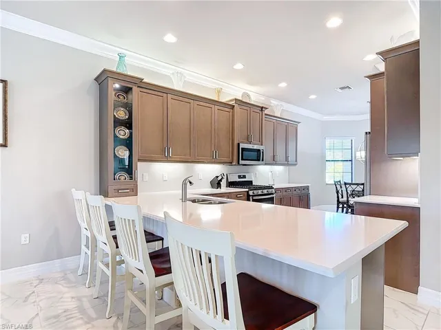 Kitchen featuring kitchen peninsula, appliances with stainless steel finishes, ornamental molding, and a kitchen bar