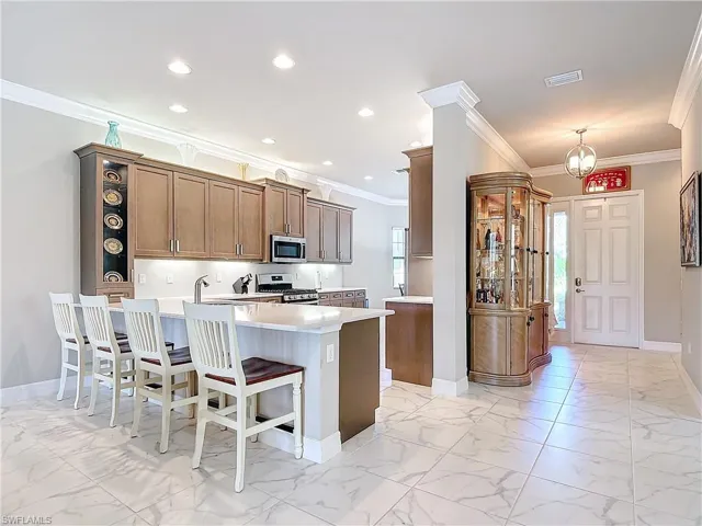 Kitchen featuring a kitchen bar, kitchen peninsula, stainless steel appliances, a notable chandelier, and ornamental molding