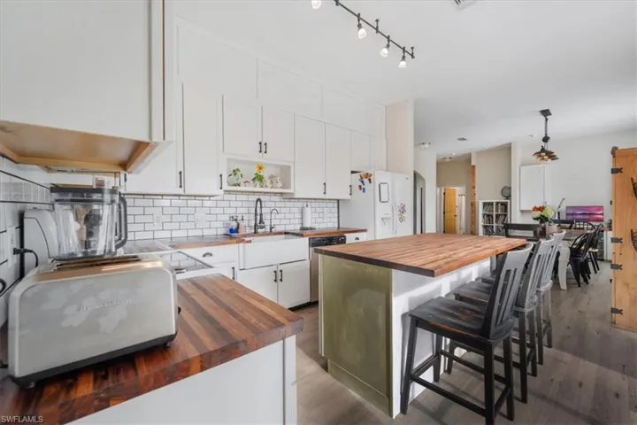 Kitchen with butcher block countertops, decorative backsplash, white cabinetry, and white fridge with ice dispenser