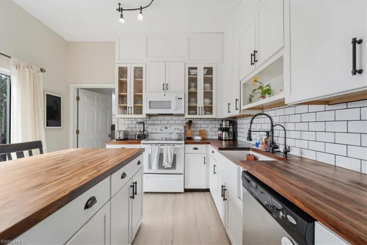 Kitchen featuring butcher block counters, tasteful backsplash, white appliances, and a sink