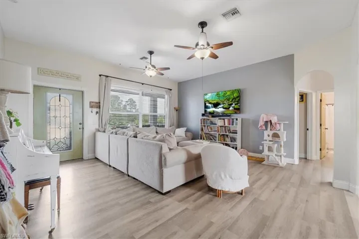 Living room with visible vents, ceiling fan, arched walkways, and light wood-style floors