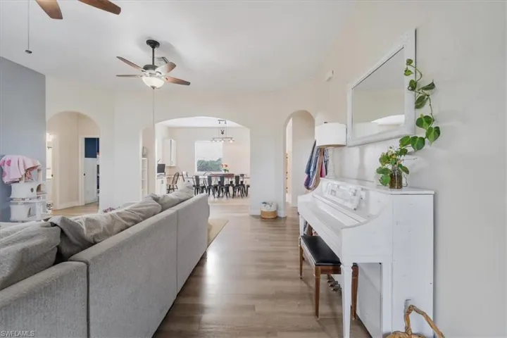 Living room with arched walkways, wood finished floors, ceiling fan, and baseboards