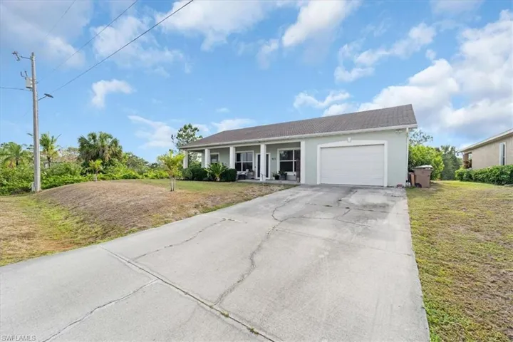 Ranch-style home with concrete driveway, stucco siding, an attached garage, a front yard, and covered porch