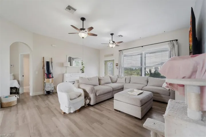 Living room with visible vents, baseboards, arched walkways, ceiling fan, and light wood finished floors