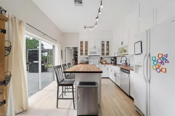 Kitchen featuring white cabinets, wooden counters, a breakfast bar, white appliances, and backsplash