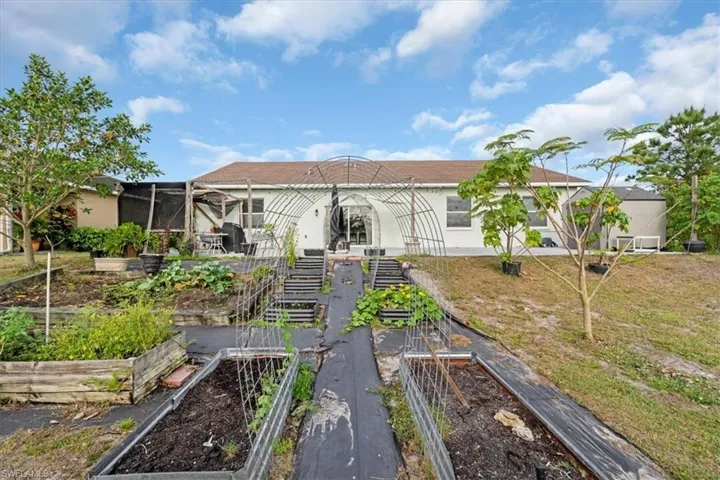 Back of property featuring stairs, stucco siding, a lawn, and a vegetable garden