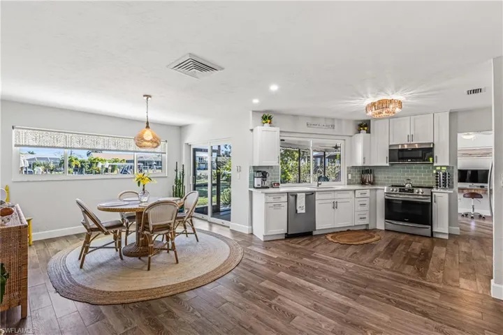 Kitchen with white cabinets, stainless steel appliances, a chandelier, tasteful backsplash, and dark wood-style flooring