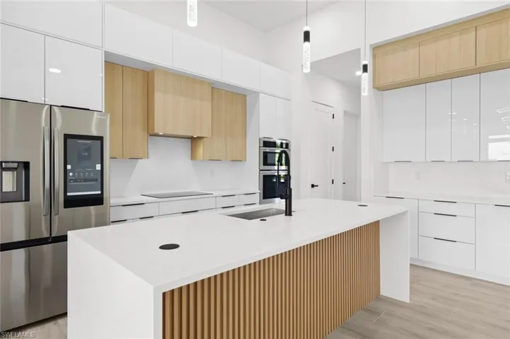 Kitchen with stainless steel appliances, light hardwood / wood-style floors, white cabinetry, and an island with sink