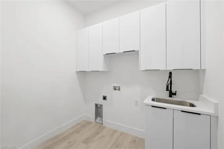 Laundry area featuring hookup for a washing machine, sink, cabinets, light wood-type flooring, and electric dryer hookup