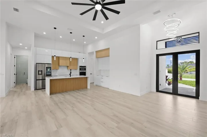 Kitchen featuring light hardwood / wood-style flooring, white cabinetry, french doors, a kitchen island with sink, and ceiling fan