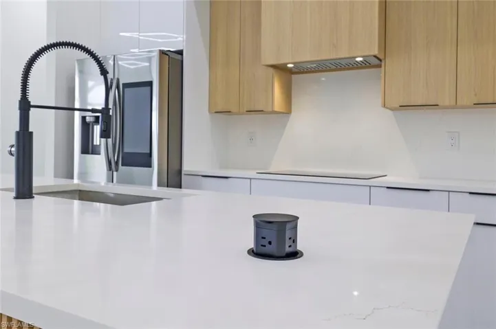 Kitchen featuring black electric cooktop, sink, decorative backsplash, light brown cabinets, and stainless steel fridge with ice dispenser