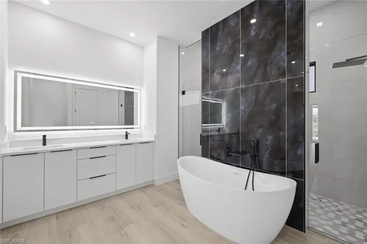 Bathroom with hardwood / wood-style floors, double sink vanity, and separate shower and tub