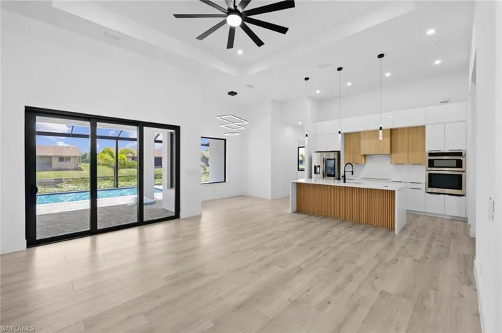 Kitchen featuring white cabinetry, sink, double wall oven, a raised ceiling, and a kitchen island with sink