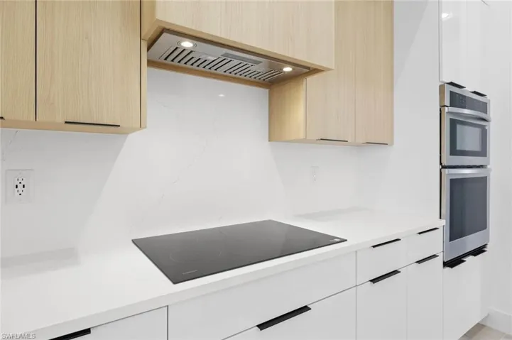 Kitchen with black electric cooktop, custom exhaust hood, double oven, and white cabinets