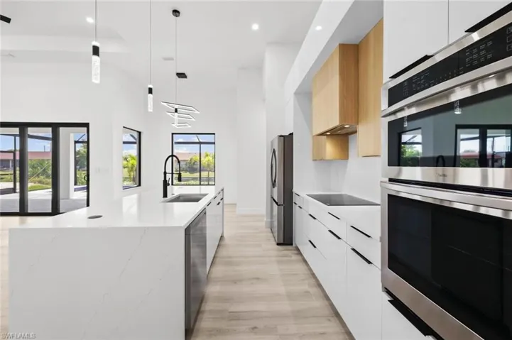 Kitchen with white cabinets, hanging light fixtures, light stone countertops, and stainless steel appliances