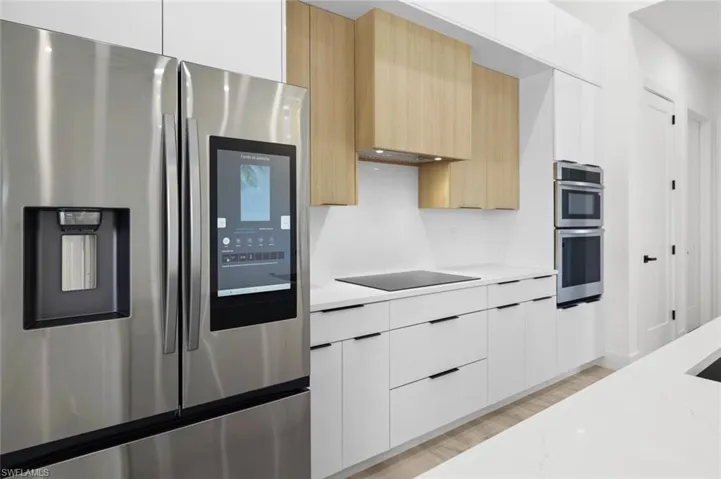 Kitchen featuring appliances with stainless steel finishes, light hardwood / wood-style flooring, light stone counters, light brown cabinetry, and white cabinetry