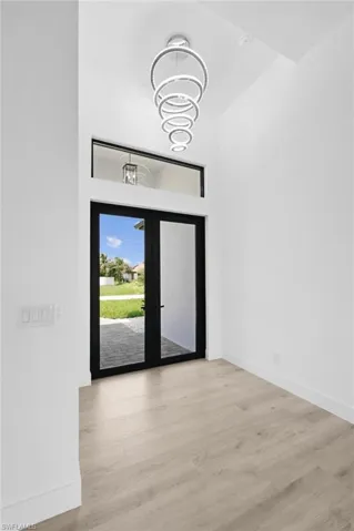 Doorway to outside featuring light wood-type flooring, french doors, and an inviting chandelier