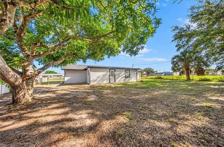 Expansive yard featuring mature trees, a chain-link fence, and a single-story exterior with a side entry door