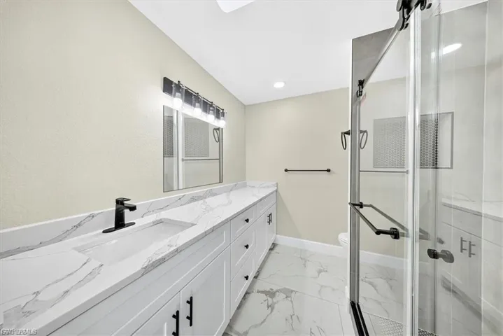 Dual-sink vanity with a white countertop, matte black hardware, and a glass-enclosed shower with a sliding door