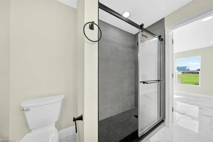 Tiled walk-in shower with a black barn door style enclosure and black penny tile floor