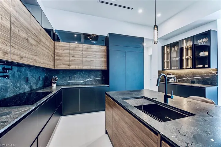 Kitchen featuring modern cabinets, dark stone counters, tasteful backsplash, glass insert cabinets, and a sink