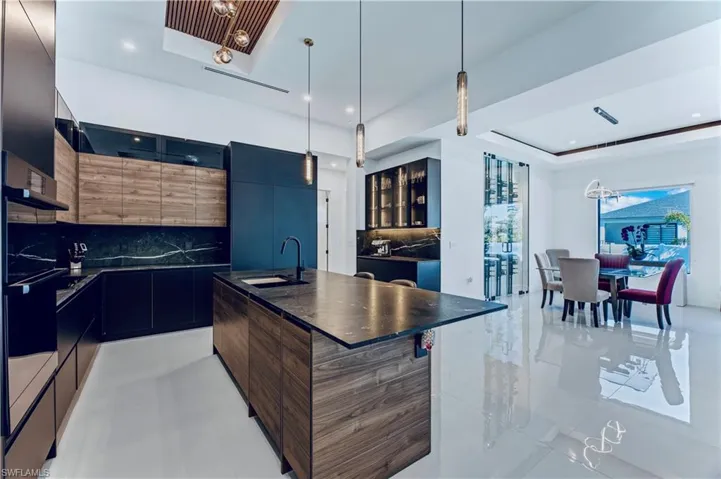 Kitchen with a center island with sink, a raised ceiling, a sink, dark countertops, and modern cabinets