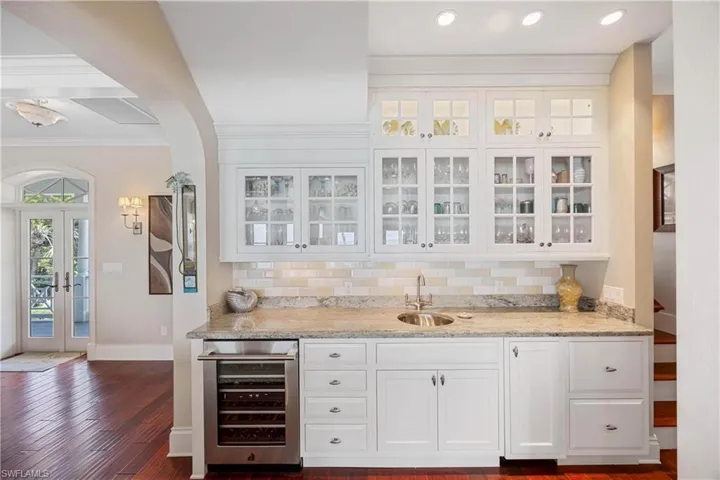 Indoor wet bar with light stone countertops, white cabinetry, beverage cooler, crown molding, and decorative backsplash