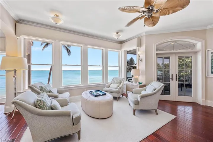 Sitting room featuring dark wood-type flooring, ornamental molding, french doors, a water view, and a ceiling fan