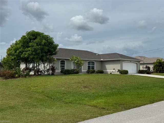 Ranch-style home featuring stucco siding, a front lawn, a garage, concrete driveway, and roof with shingles
