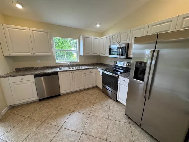 Kitchen featuring appliances with stainless steel finishes, white cabinets, light tile patterned floors, vaulted ceiling, and recessed lighting