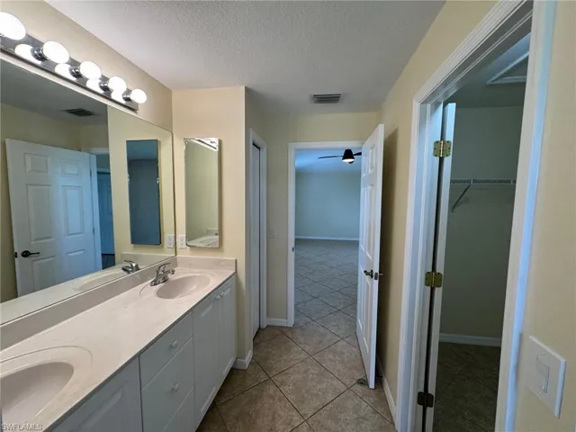 Primary Bathroom with double vanity, a textured ceiling, light tile patterned floors, a spacious closet, and ceiling fan
