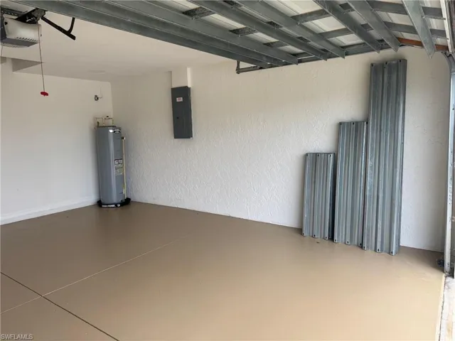 Garage with a textured wall, electric panel, electric water heater, and a garage door opener