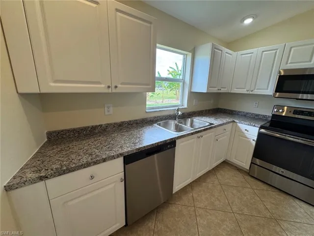 Kitchen with stainless steel appliances, white cabinetry, light tile patterned flooring, and lofted ceiling