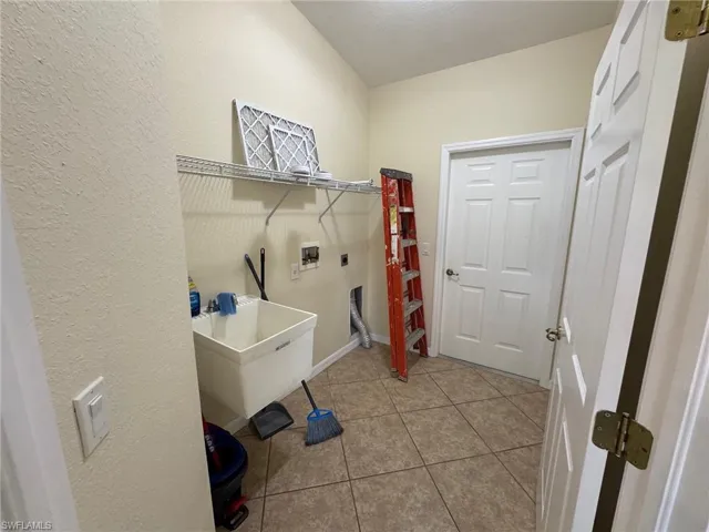 Laundry area featuring light tile patterned floors, electric dryer hookup, a textured wall, and hookup for a washing machine